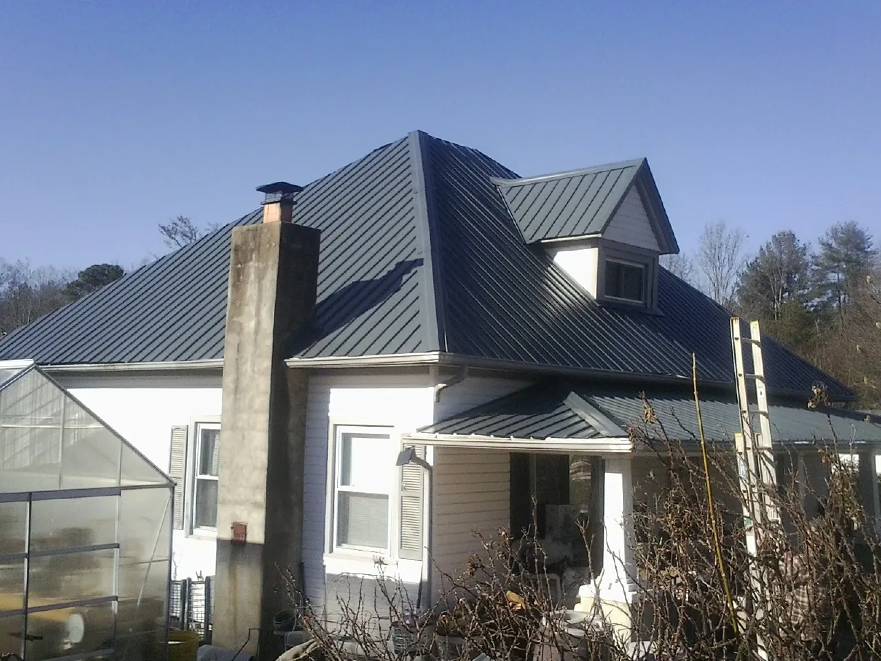 Dark blue standing seam metal roof on a white farmhouse with dormer — Slate & Tile Roof Repair by Roofing Brothers in Clifford