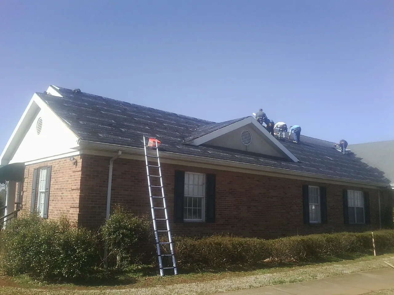 Crew tearing shingles off a brick ranch roof with a ladder set — Metal Roof Repair work by our crew in Clifford