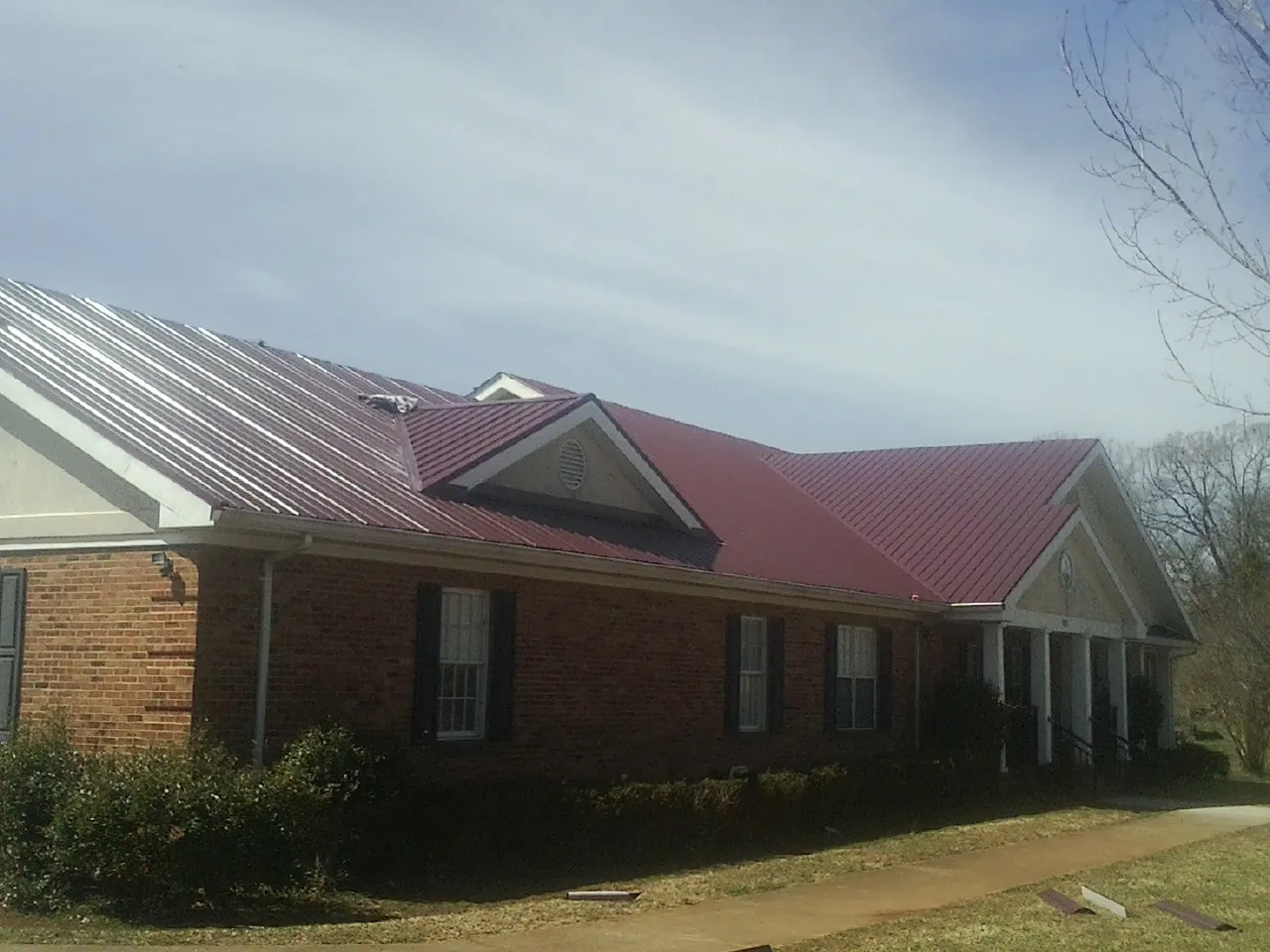 Red metal roof with gabled entries on a long brick building, from a Hail Damage Roof Repair job in Clifford
