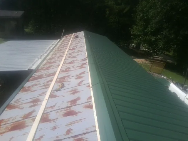 Old rusted panels beside newly installed green metal roofing — Wind Damage Roof Repair by Roofing Brothers in Clifford