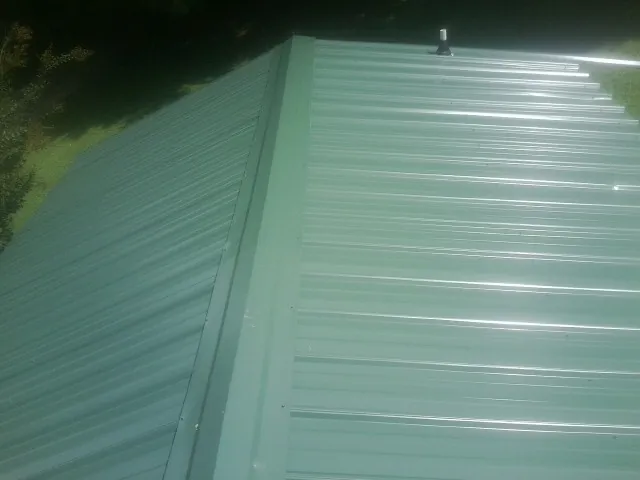 New green metal panels meeting at the ridge of a roof — Flat Roof Repair work by our crew in Clifford