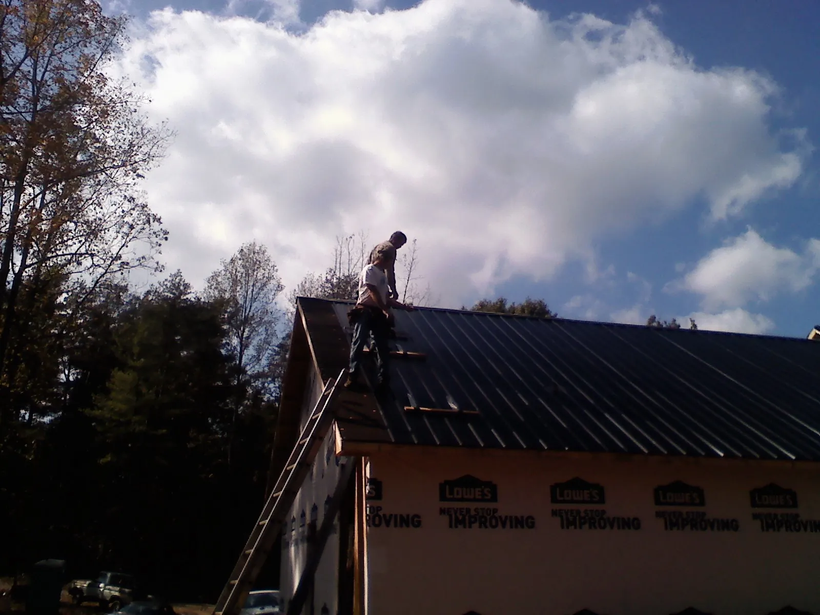 Roofer fastening dark metal panels high against a cloudy sky, from a Roof Inspection job in Clifford