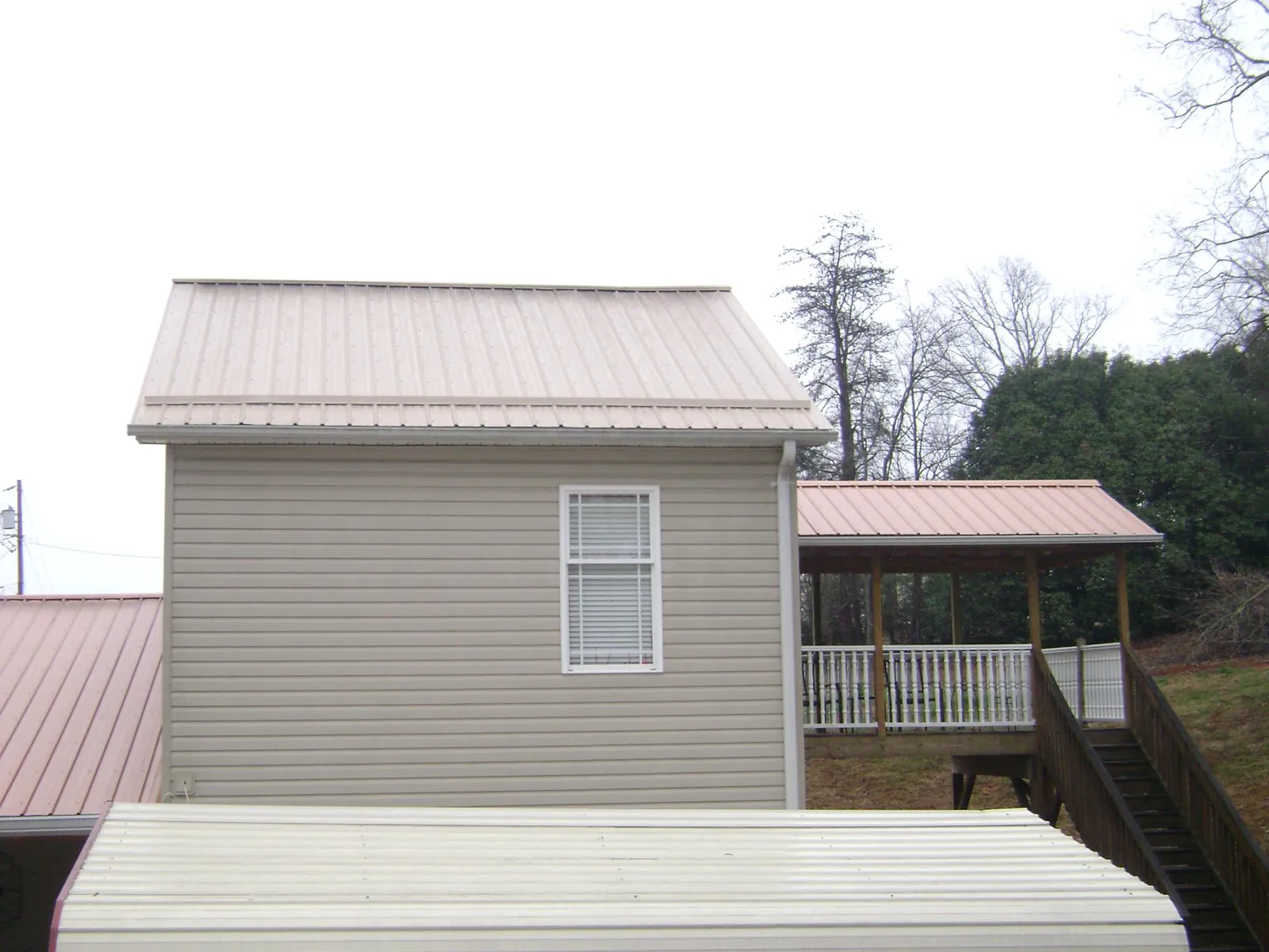 Tan metal roofs on a two story addition and attached porch, from a Roof Replacement job in Clifford